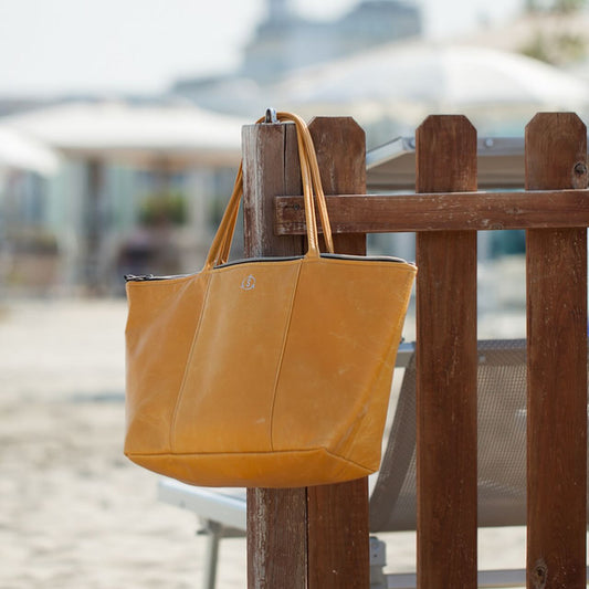 A Smateria mustard yellow Daydreamer tote bag hanging on a wooden railing at a beachside location.