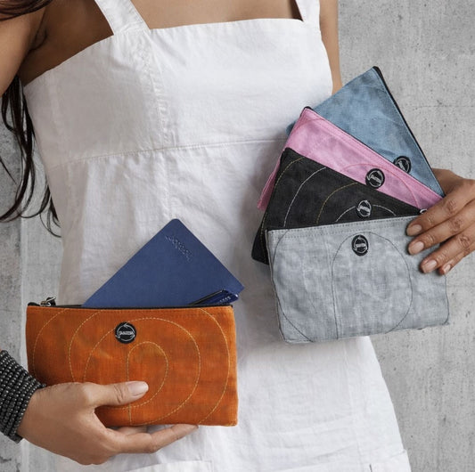 A person holding 5 smateria router pouches in red, silver, black, transparent pink and transparent blue net with a notebook and pen in the red pouch