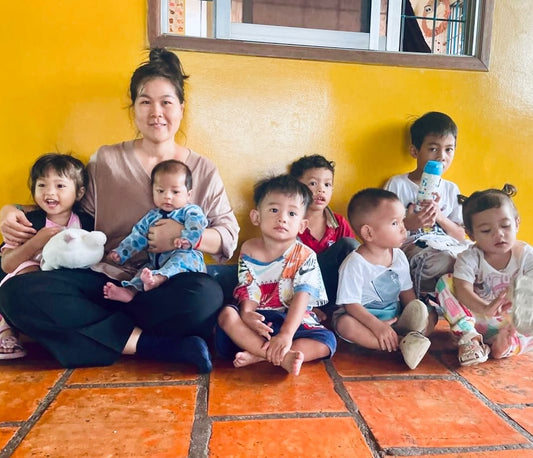 Ary sitting with her children and other children of Smateria team members outside the onsite daycare, showing the supportive community around the workshop.