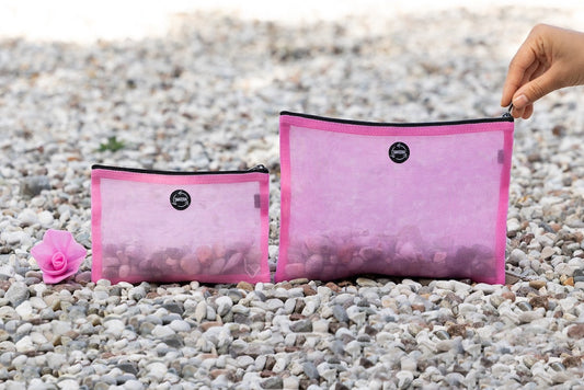 Two Smateria Alpha pouches placed on a rocky shoreline, showcasing their transparent net fabric and practical size.