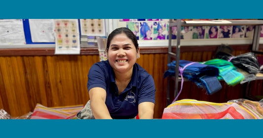 Smateria team member leaning over net fabric at the workshop, smiling as she works, highlighting the people and care behind every ethically made bag.