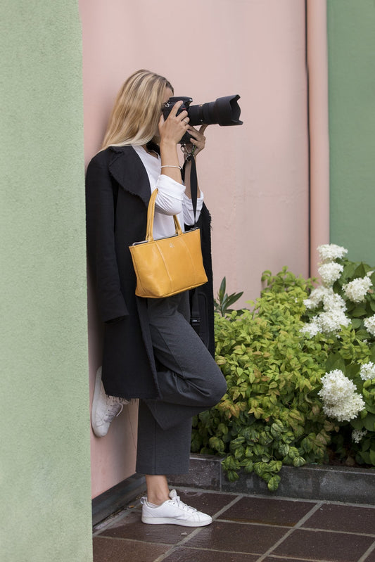 A woman taking a photo holding a Smateria Daydreamer tote bag in mustard ellow