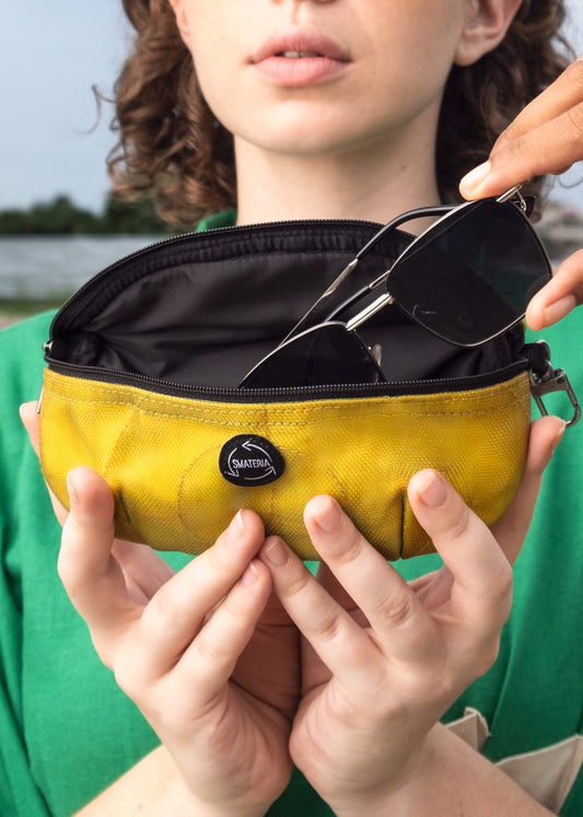 A person holding a small yellow and black sunglasses pouch with a zipper.