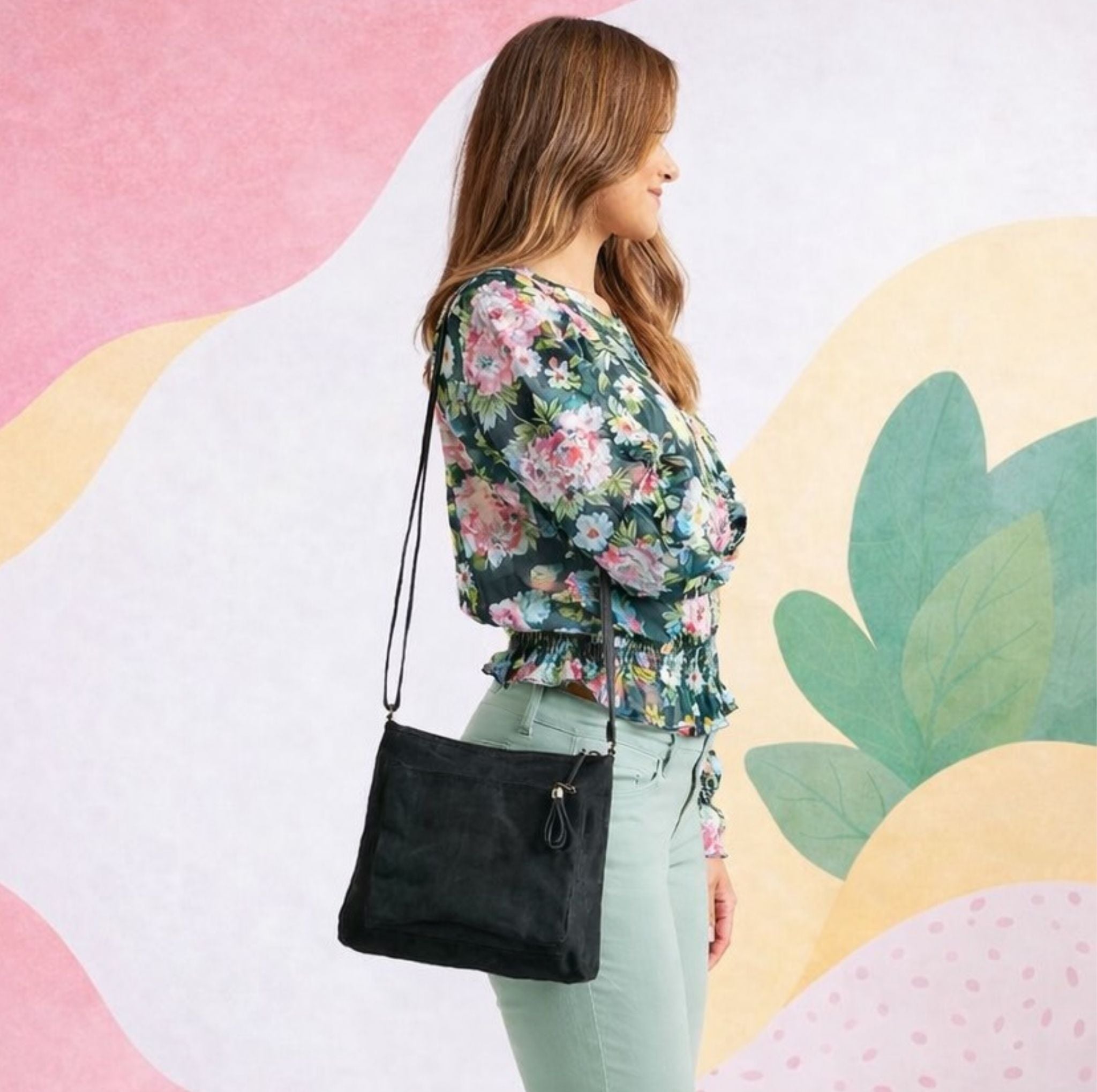 Woman wearing a floral blouse and holding a black smateria crossbody bag against a colorful abstract background