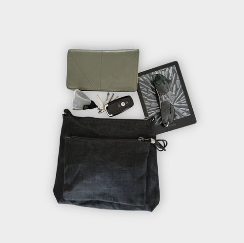 Black Smateria bustle crossbody bag with a grey purse and items on a light grey background