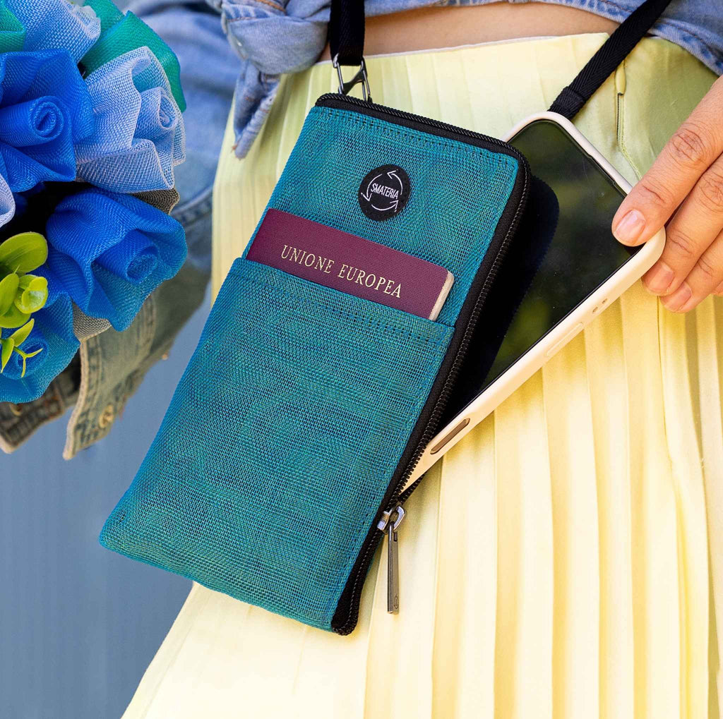 Smateria Key crossbody phone bag with phone and passport held by a person, with flowers in the background