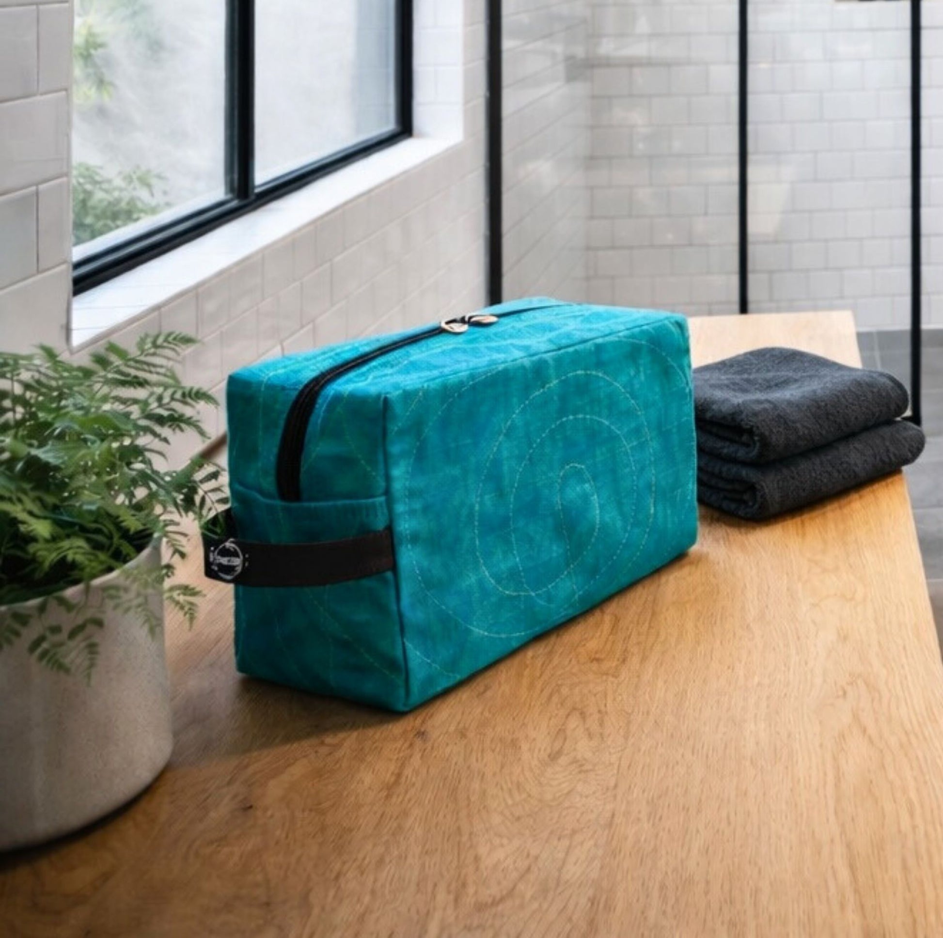 A Smateria RAM Vanity bag on a wooden bench with black towels and a plant in the background.