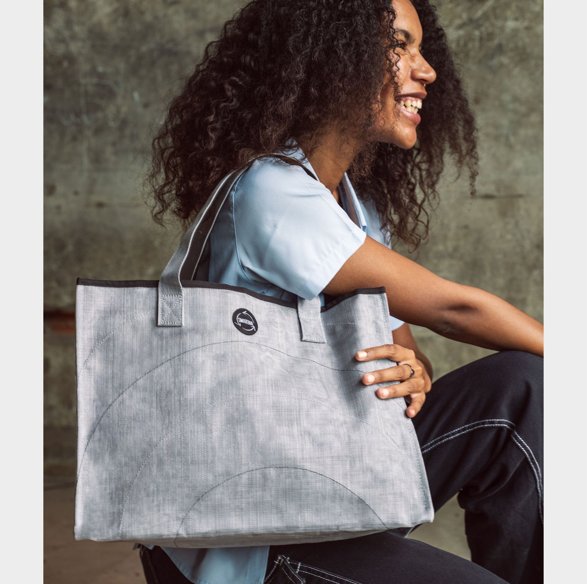 Woman holding a Smateria Silver shopper  tote bag against a concrete wall.