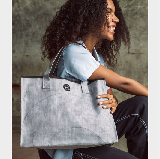 Woman holding a Smateria Silver shopper  tote bag against a concrete wall.